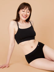 Woman sitting in black cotton briefs, looking relaxed and smiling.